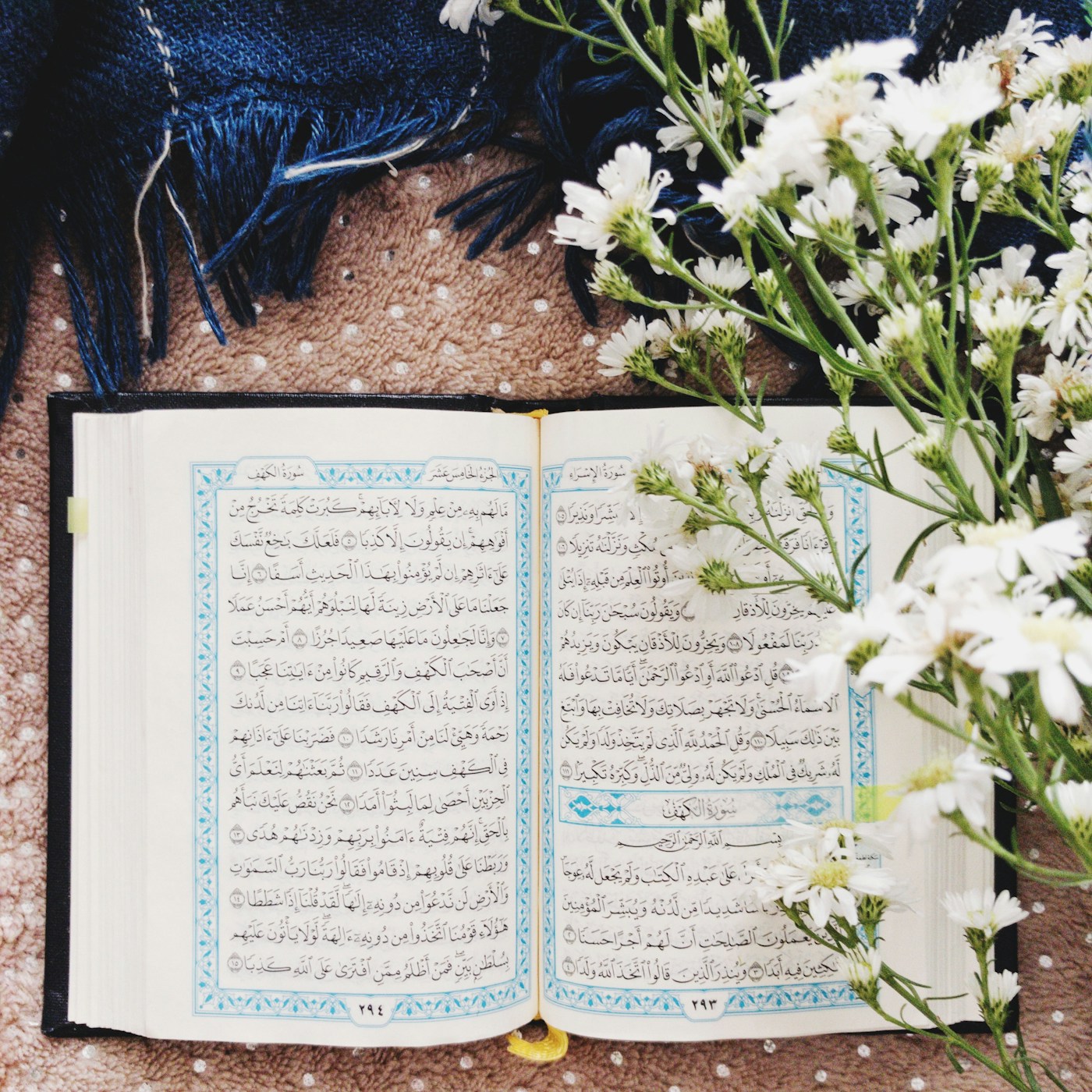 An open Quran on a wooden table beside white flowers